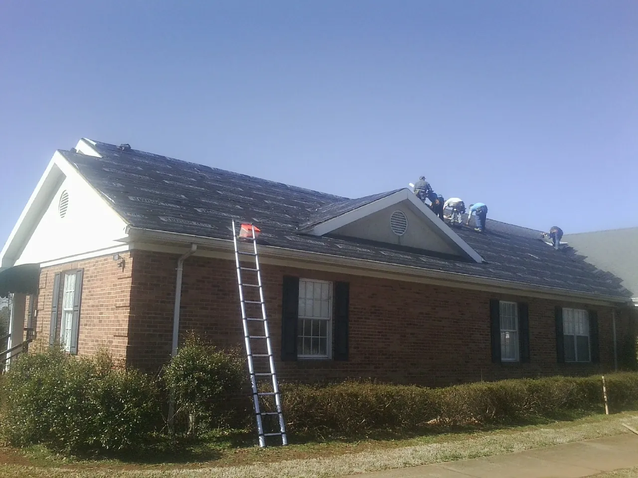 Crew tearing shingles off a brick ranch roof with a ladder set — Emergency Roof Repair work by our crew in Parkesburg