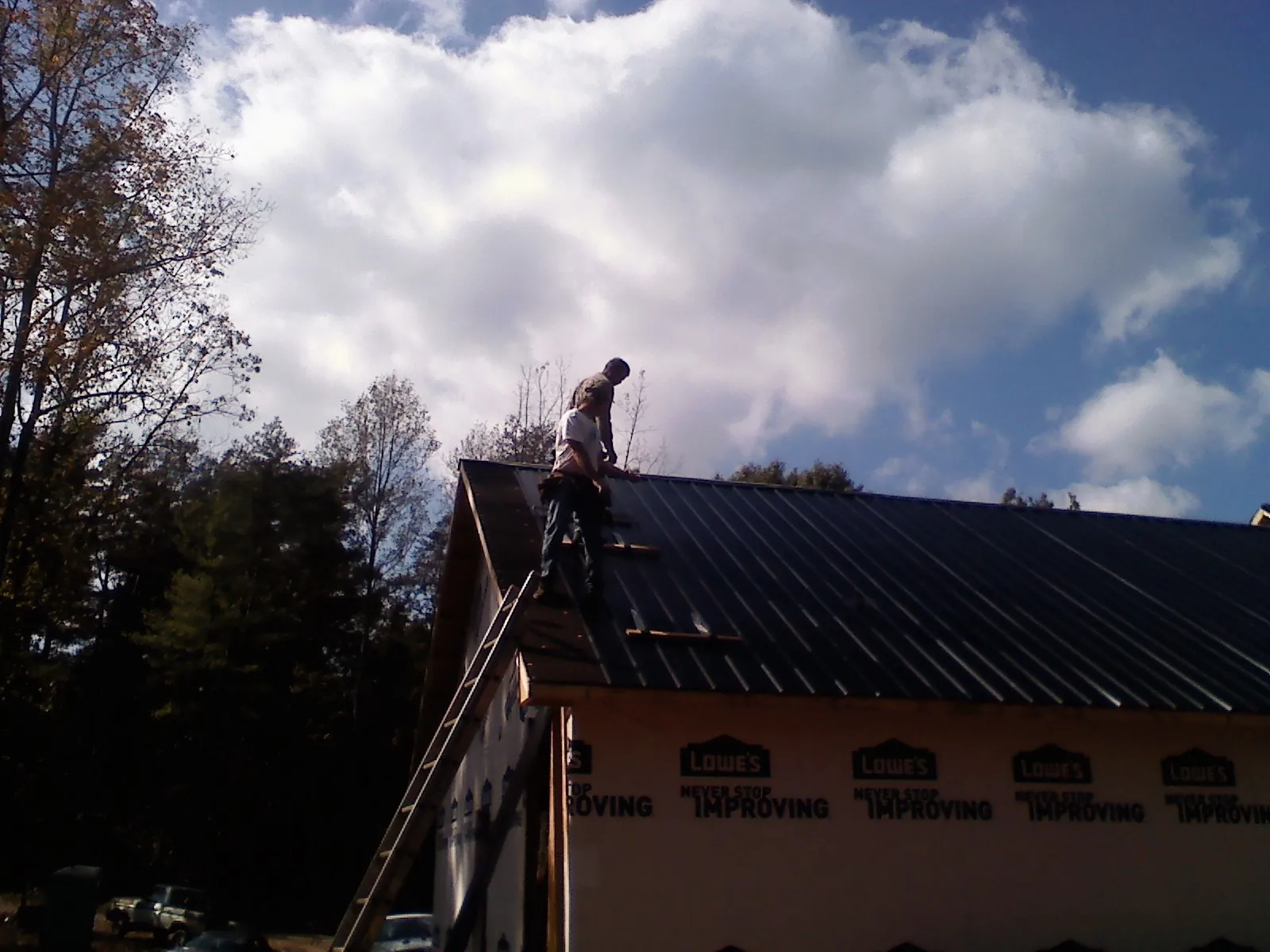 Roofer fastening dark metal panels high against a cloudy sky, from a Roof Inspection job in Parkesburg