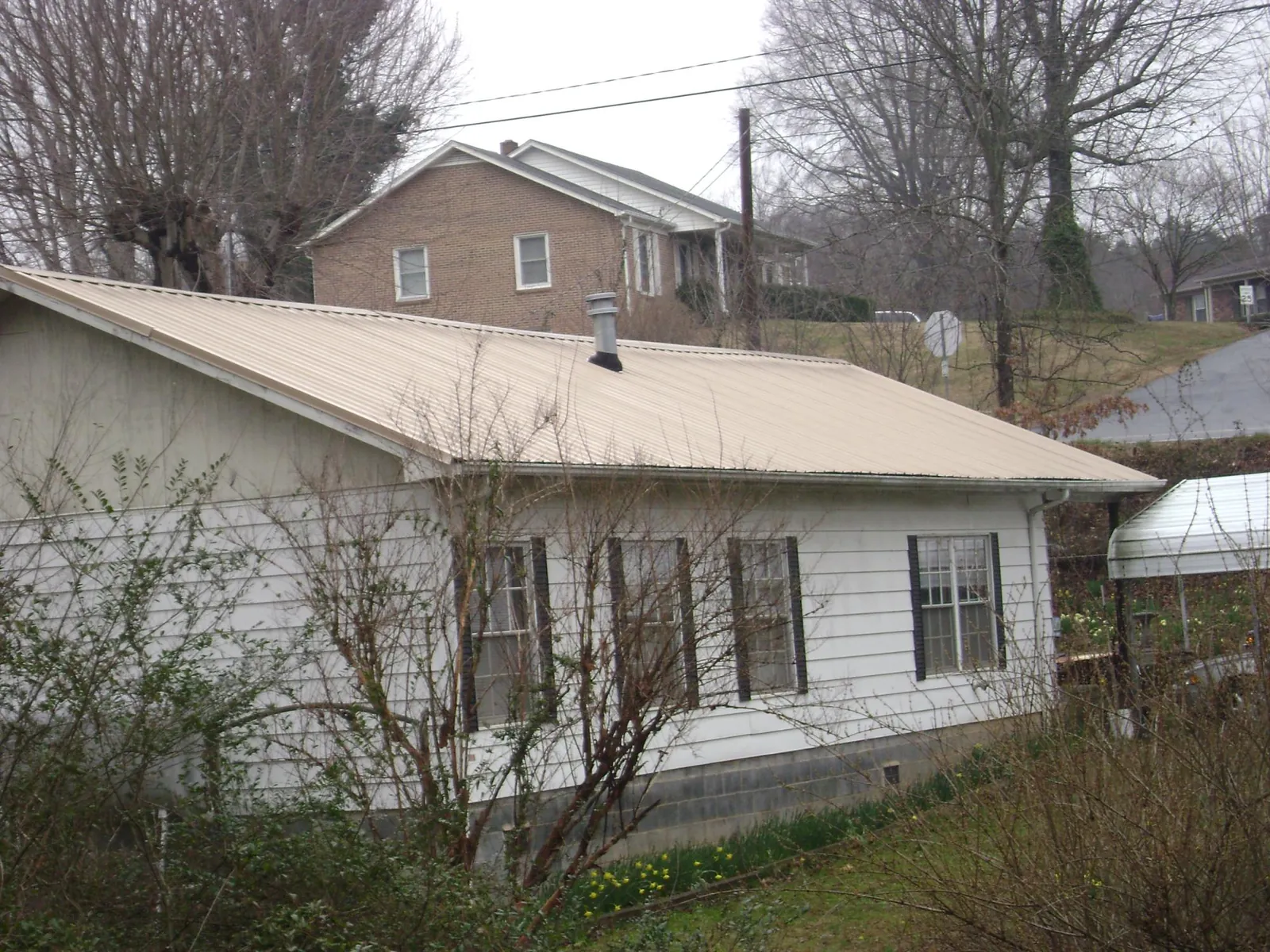 Tan metal roof on a white sided house set into a hillside — Commercial Roofing by Roofing Brothers in Parkesburg